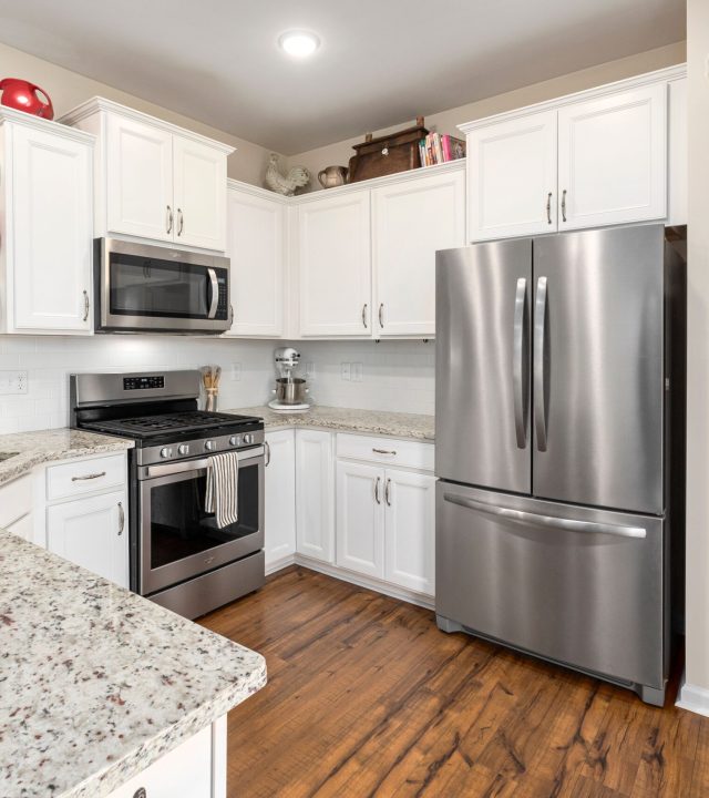 Bright modern kitchen featuring white cabinets and stainless steel appliances, including a refrigerator and stove.
